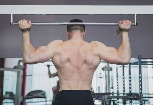 athlete pulls up in the gym fastening hands on the horizontal bar.