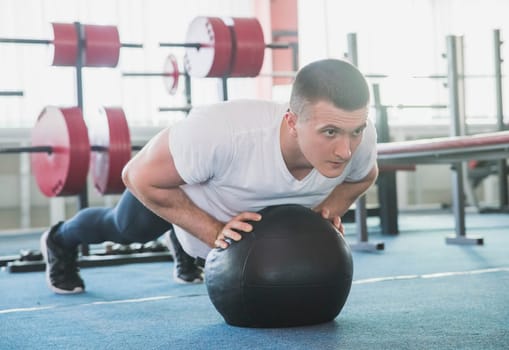 athlete push ups on a black ball in the gym.