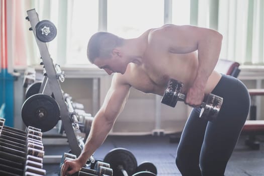 Athlete trains back muscles by lifting a dumbbell.