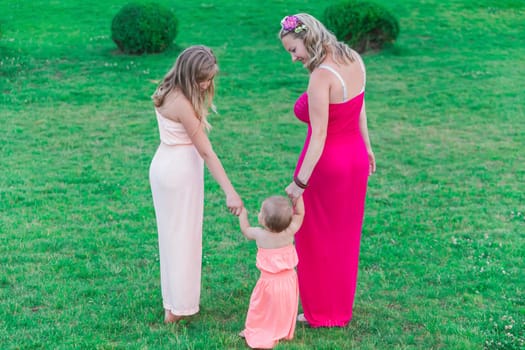 mom with two daughters dressed in similar dresses walks in the park.