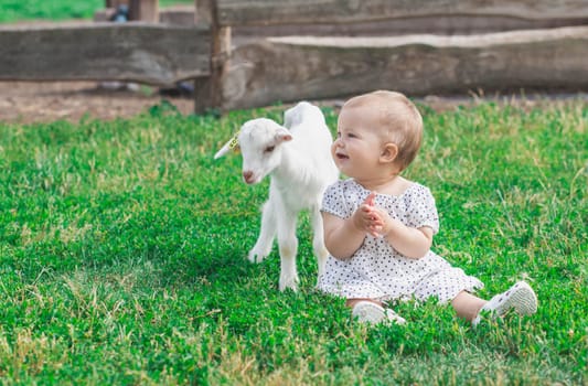 beautiful baby in a pea dress plays with a goat on a farm.