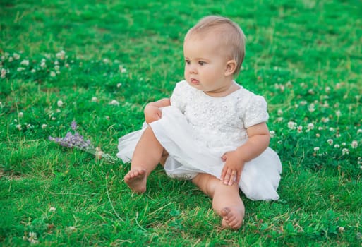 beautiful baby in white dress sitting on the lawn.