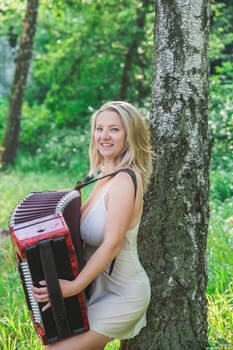 beautiful blonde in a nightgown plays accordion in the woods.