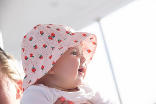 charming newborn girl in hat looks at the sunset and smiles toothlessly