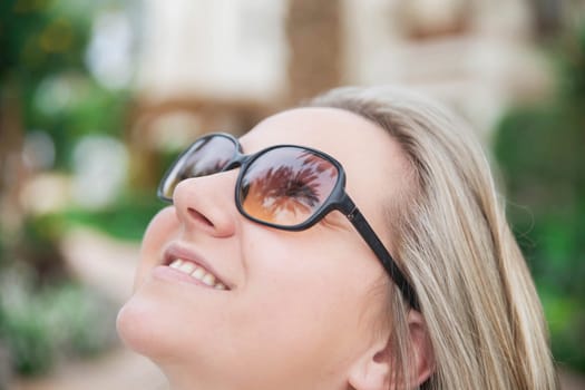 attractive woman in sunglasses looking up and in her glasses palm trees are reflected