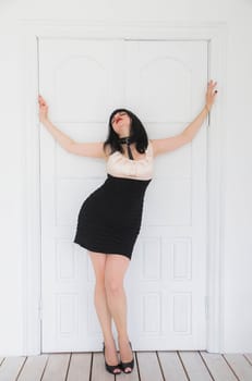 sexy brunette in a short dress stands near white doors.