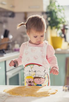 Adorable baby in an apron makes cookies from dough in the kitchen.
