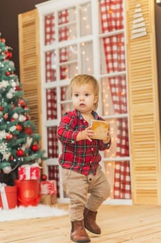 cute baby in trousers and a plaid shirt plays on the floor with wooden cube