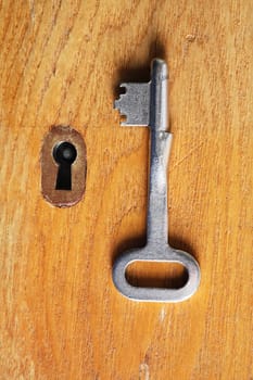 One metal key near keyhole on wooden background
