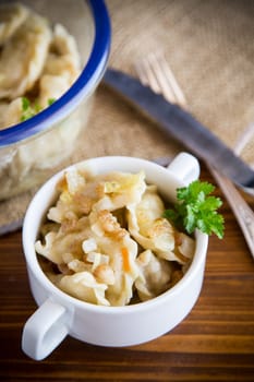 cooked dumplings with potatoes and fried onions, in a bowl on a wooden table.