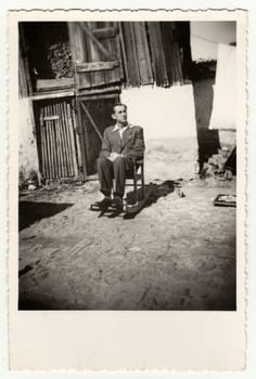 THE CZECHOSLOVAK REPUBLIC - SEPTEMBER 20, 1942: Retro photo shows a young man sits on the rocking chair in the backyard. Vintage black and white photography.