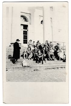 KUTNA HORA, THE CZECHOSLOVAK SOCIALIST REPUBLIC - APRIL 25, 1954: Retro photo shows a group of people sits on stairs outside. Vintage black and white photography.