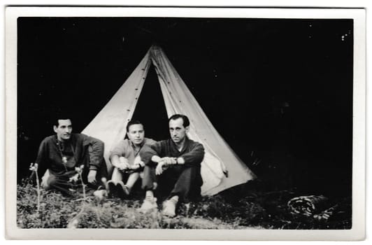 THE CZECHOSLOVAK SOCIALIST REPUBLIC - JULY 13, 1956: Retro photo shows tourists outside. Tramps - wanderers sit in front of tent. Summer vacation theme. Vintage black and white photography.