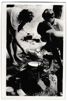 THE CZECHOSLOVAK SOCIALIST REPUBLIC - JULY 13, 1956: Retro photo shows tourists outside. Tramps -wanderers make food on open fire. Summer vacation theme. Vintage black and white photography.