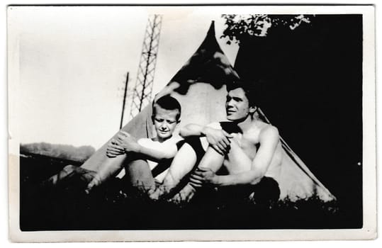 THE CZECHOSLOVAK SOCIALIST REPUBLIC - AUGUST 11, 1956: Retro photo shows tourists outside. Tramps -wanderers sit in front of a tent. Summer vacatoin - holiday theme. Vintage black and white photography.