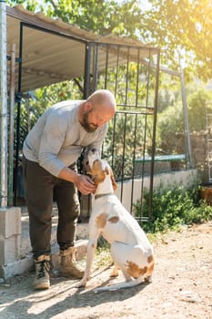Vertical portrait of a man stroking a dog in the yard of a house