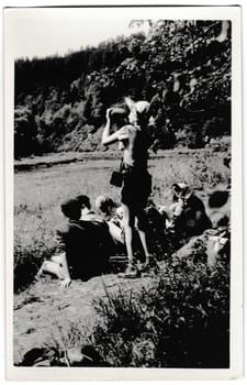 THE CZECHOSLOVAK SOCIALIST REPUBLIC - CIRCA 1950s: Retro photo shows tourists outside. The boy drinks water from water-flask. Vintage black and white photography.