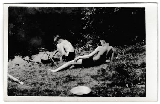 THE CZECHOSLOVAK SOCIALIST REPUBLIC - CIRCA 1950s: Retro photo shows tourists outside. The boys make food in camping pot. Vintage black and white photography.