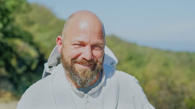 Portrait of a happy beekeeper wearing protective clothes in a field in a sunny day