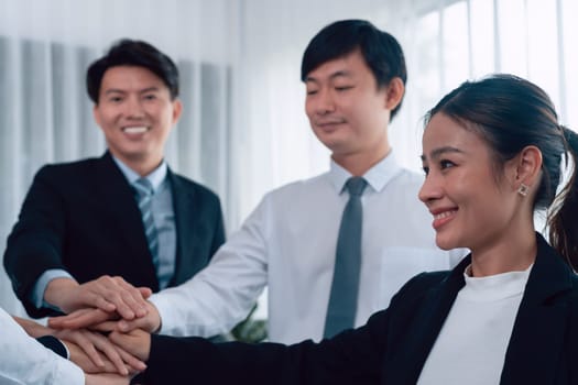 Closeup business team of suit-clad businessmen and women join hand stack together and form circle. Colleague collaborate and work together to promote harmony and teamwork concept in office workplace.