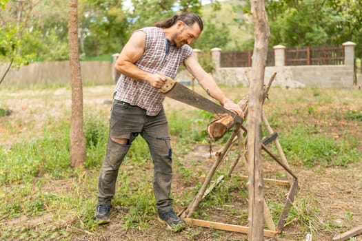 Woodcutter sawing wood with a hand saw in an orchard
