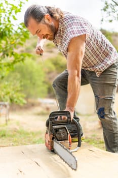 Vertical portrait of a woodcutter using a electric chainsaw in a garden