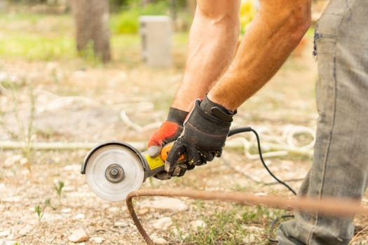 Detail of the hands of a man using gloves to cutting iron with a radial saw