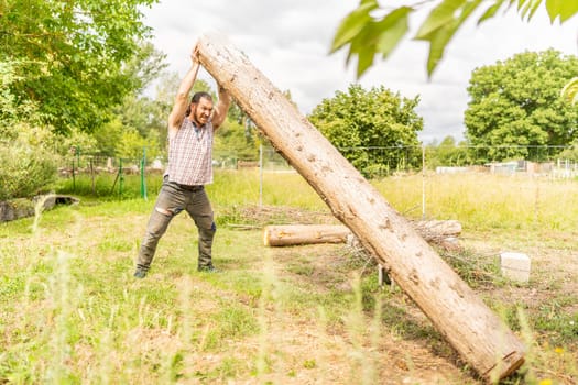 Portrait of a male woodcutter lifting a log with his bare hands in a field
