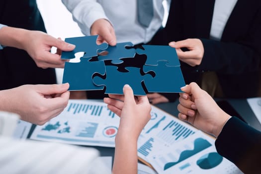 Closeup top view business team of office worker putting jigsaw puzzle together over table filled with financial report paper in workplace with manager to promote harmony concept in meeting room.