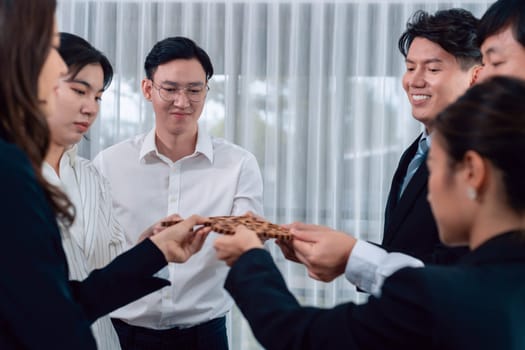 Closeup hand holding wooden gear by businesspeople wearing suit for harmony synergy in office workplace concept. Group of people hand making chain of gears into collective form for unity symbol.