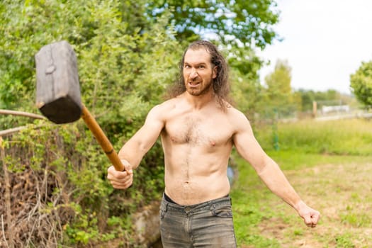 Portrait of a country man with bare torso and wild expression with a hammer