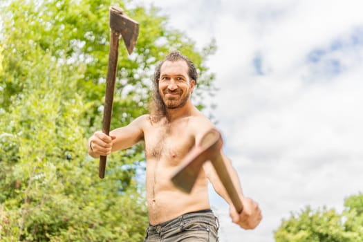 Low angle portrait of a smiley wild man with bared torso with two axes