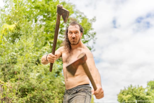 Low angle portrait of a wild man with bared torso with two axes