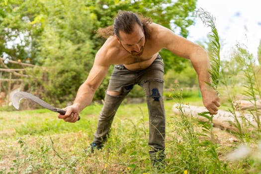 Low angle view of a caucasian strong man cutting grass with a sickle