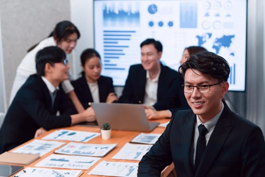 Focus portrait of successful confident male manager or executive in business wear with blurred background of businesspeople, colleagues working with financial report papers in office of harmony.