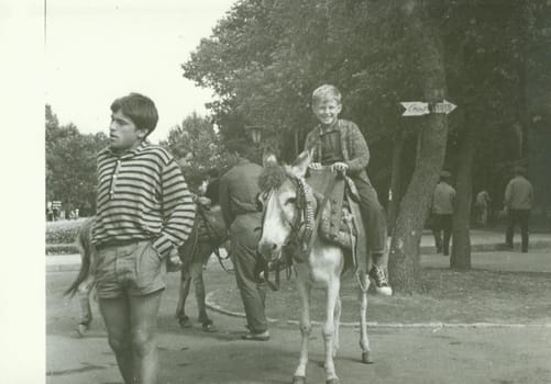 USSR - CIRCA 1970s: Retro photo shows boy rides on donkey in the park. Vintage black and white photography.