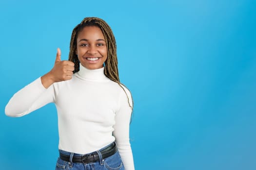Studio portrait with blue background of an african woman gesturing positively with the thumb up