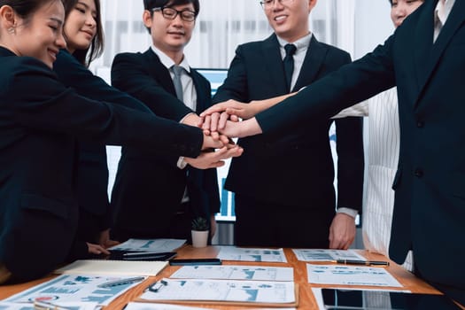 Closeup business team of suit-clad businessmen and women join hand stack together and form circle. Colleague collaborate and work together to promote harmony and teamwork concept in office workplace.