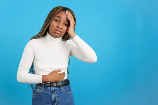 Studio portrait with blue background of an african woman touching her belly with her hand gesturing bodily discomfort