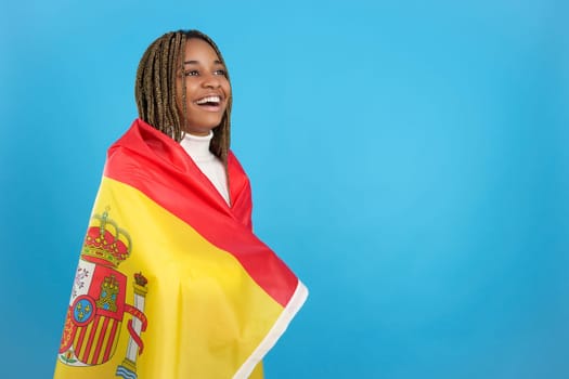 Studio portrait with blue background of a happy african woman wrapped in a spanish national flag