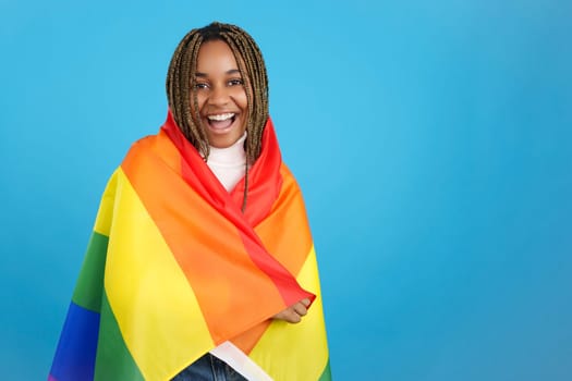 Studio portrait with blue background of a proud african woman wrapped in a lgbt rainbow flag