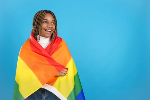 Studio portrait with blue background of a happy african woman wrapped in a lgbt rainbow flag