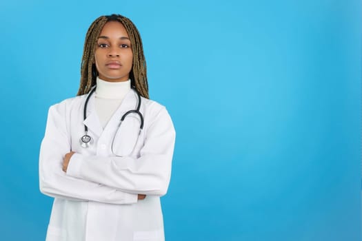 Studio portrait with blue background of a serious african female doctor with arms crossed looking at camera
