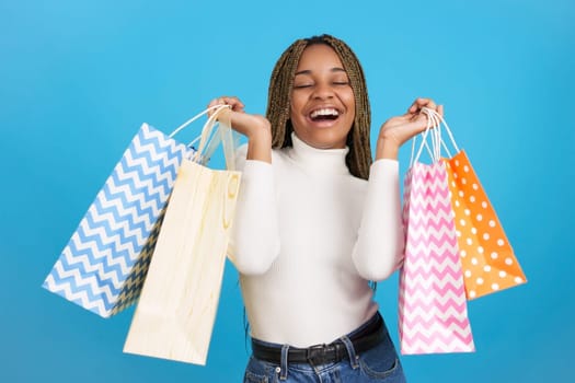 Studio portrait with blue background of an excited African woman with the eyes closed carrying many shopping bags