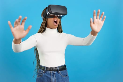 Studio portrait with blue background of a shocked african woman wearing virtual reality goggles