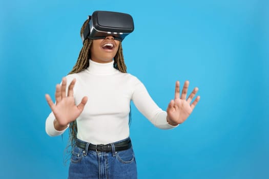 Studio portrait with blue background of a smiling african woman gesturing with hands while using a virtual goggles