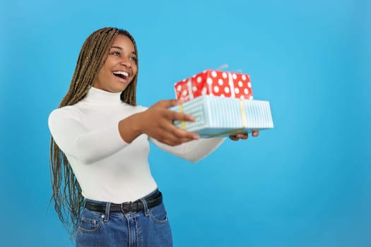 Studio portrait with blue background of a happy casual african woman delivering a gift
