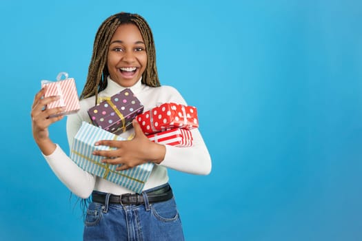 Studio portrait with blue background of a happy african woman looking at camera while receiving many gifts