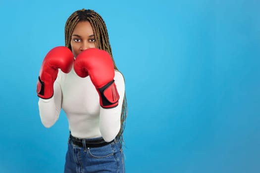 Studio portrait with blue background of a african woman with boxing gloves and fighting pose