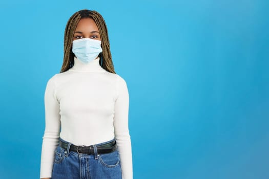 Studio portrait with blue background of an african woman looking at camera while using a protective face mask